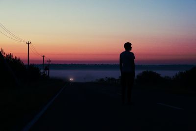 Rear view of silhouette man standing on orange sunset sky