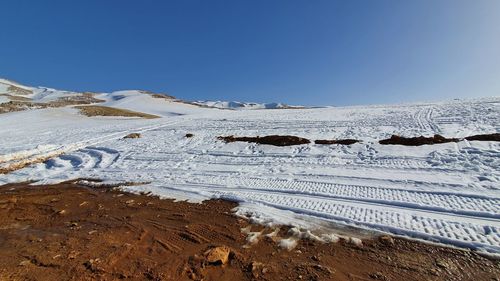 Snow covered landscape against clear blue sky