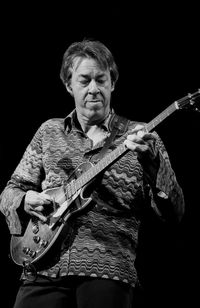 Portrait of a young man playing guitar against black background