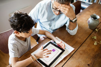 High angle view of boy using digital tablet while sitting with father at home