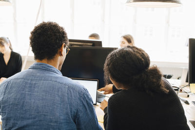 Rear view of coworkers discussing coding over laptop on desk in office