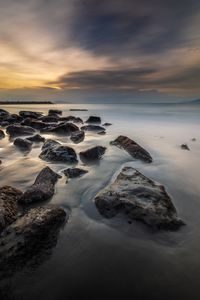 Rocks on beach against sky during sunset