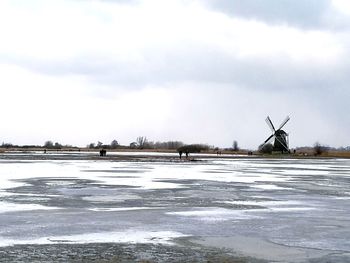 Traditional windmill by lake against sky