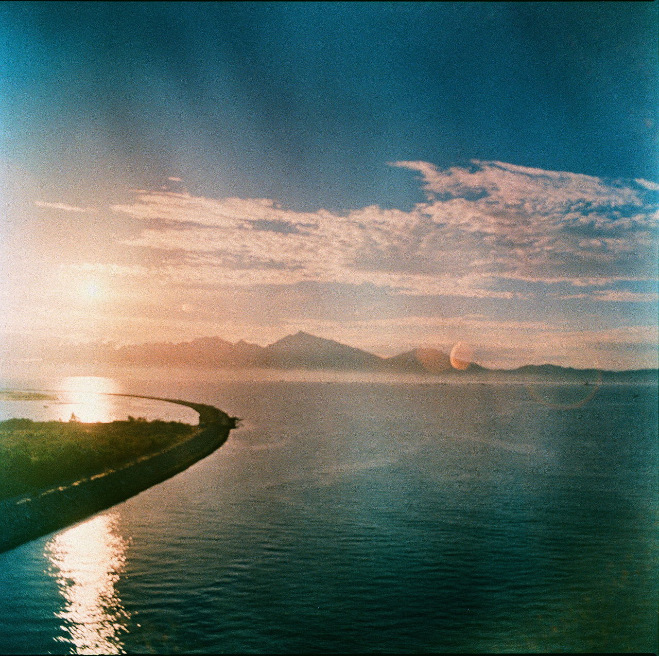 SCENIC VIEW OF SEA AGAINST MOUNTAIN DURING SUNSET