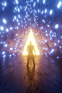 Rear view of silhouette man standing in illuminated tunnel