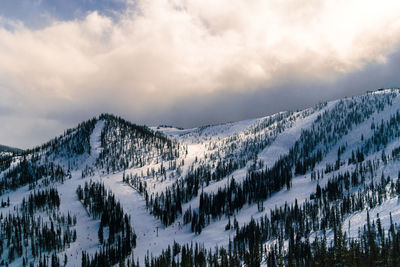 Scenic view of snowcapped mountains against sky with skiers