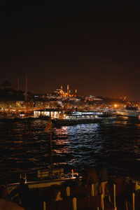 Illuminated buildings by sea against clear sky at night