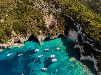 Aerial view of sailing yachts at anchor at paxos blue cave with turquoise water and anchored yachts.