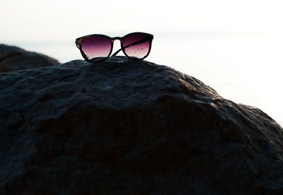 Close-up of sunglasses on rock against sky