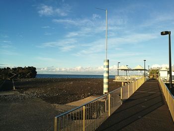 Empty footpath by sea against blue sky