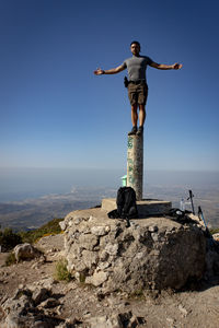 Man standing on rock by sea against clear sky