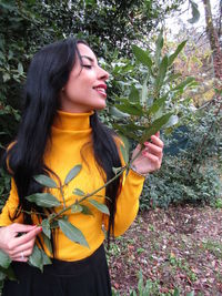 Young woman holding plant while standing against plants