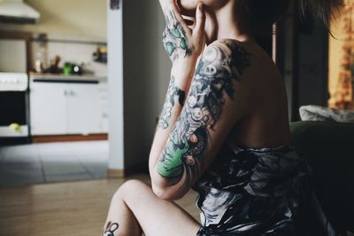 Midsection of woman with tattoo sitting at home