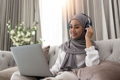 Young woman using laptop while sitting on sofa at home