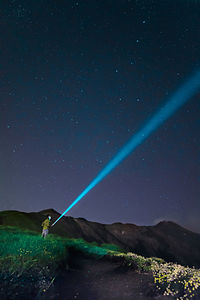 Hiker with flash light standing on field against sky