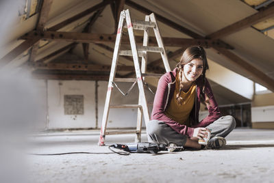 Young woman having coffee near ladder at home