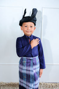 Portrait of cute boy wearing traditional clothing standing against wall