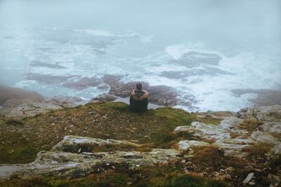 Woman sitting on rock by sea against sky