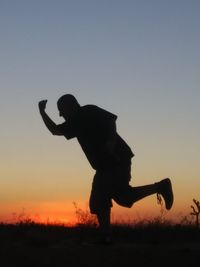 Silhouette man standing on field against sky during sunset