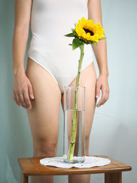 Midsection of woman standing by flower vase on table