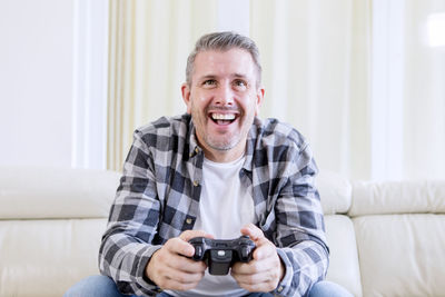 Smiling man playing video game while holding remote control on sofa at home