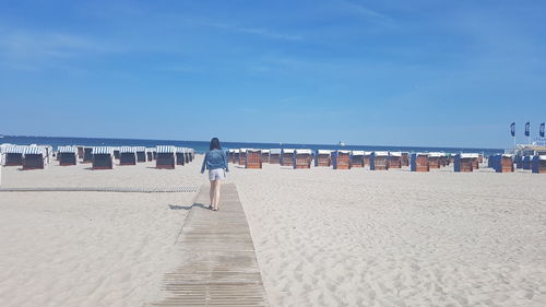 Rear view of woman walking on boardwalk on beach
