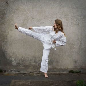 Young woman practicing karate against wall