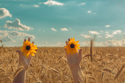 Cropped hand of woman holding yellow flower against sky