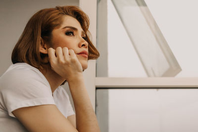 Portrait of young woman looking away against wall