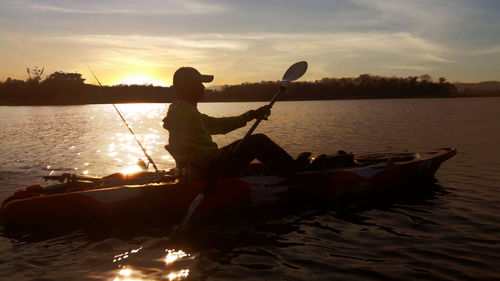 Silhouette person in lake against sky during sunset