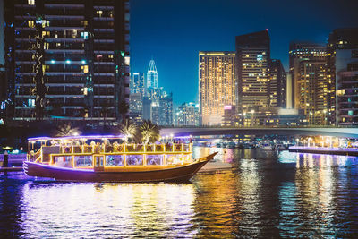 Illuminated buildings by river against sky at night