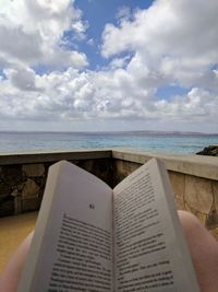 Low section of person on book by sea against sky