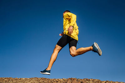 Low angle view of person jumping against clear blue sky