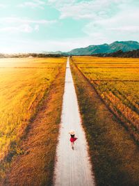 High angle view of woman walking on road amidst field against sky