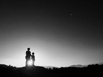 Silhouette people standing on rock against clear sky during sunset