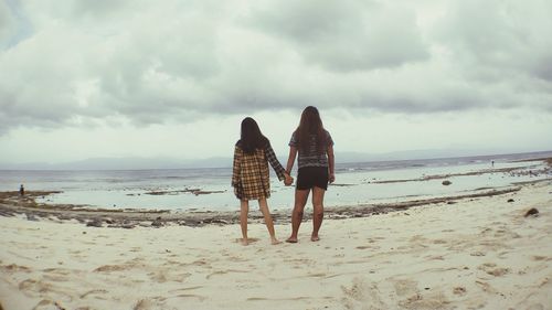 Rear view of women on beach against sky