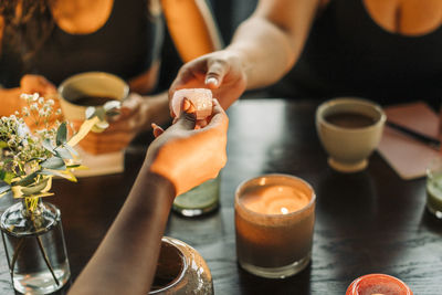 Hand of woman passing crystal to female friend over burning candle at retreat center