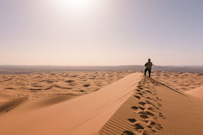 Rear view of man walking on sand against sky