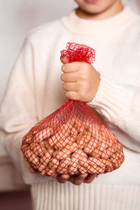 A girl in a cream sweater holds a mesh bag with peanuts in a shell. lifestyle