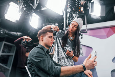 Young man is preparing for tv online broadcast. woman helps with make up.