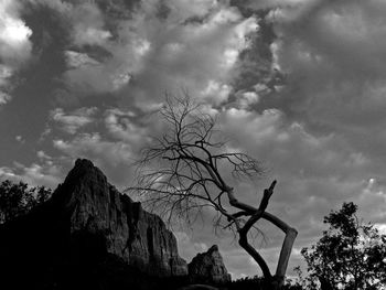 Low angle view of bare trees against cloudy sky