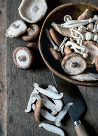 Top view of wooden bowl full of shiitake mushrooms on wood table with knife on top