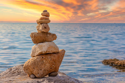 Stack of pebbles on shore against sunset sky