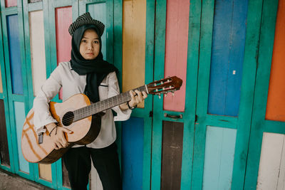 Full length portrait of woman playing guitar against wall