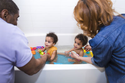 Parents bathing daughters together in bathtub