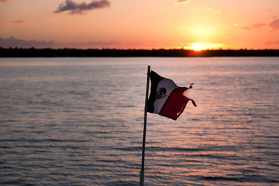 Flag on lake against sky during sunset