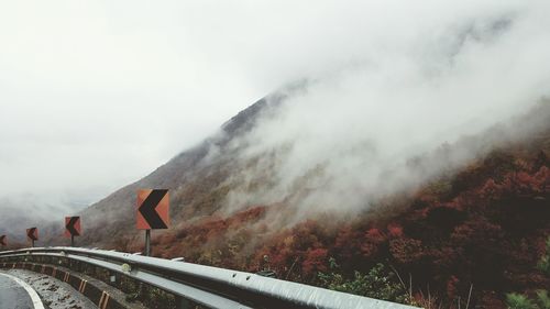 Arrow signs amidst road and mountain during foggy weather