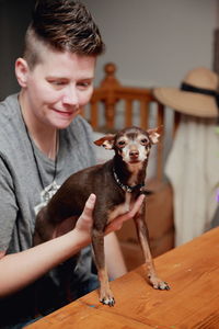 Mid adult woman holding chihuahua dog on table