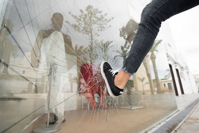 Low angle of crop unrecognizable male vandal breaking showcase of store in city