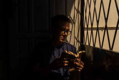 Young man reading book while sitting by gate